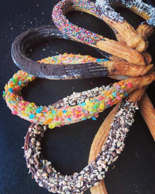 A colorful assortment of churros coated in various toppings, arranged in a playful, intertwined pattern.