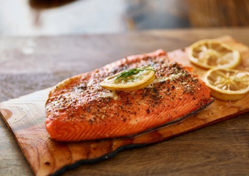 A perfectly cooked salmon fillet garnished with lemon slices on a wooden cutting board.