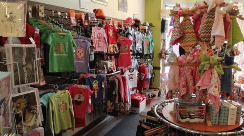 A colorful children's clothing store displaying various shirts, dresses, and accessories on racks and hangers.