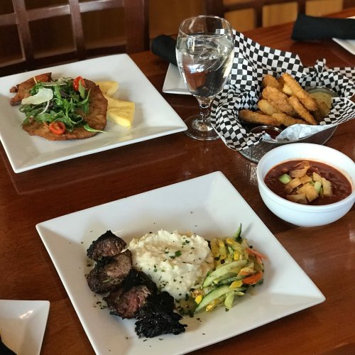 A table setting with a plate of steak, mashed potatoes, sautéed vegetables, a salad, and a side of fried food.