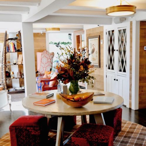 A cozy interior featuring a round table with a floral centerpiece, surrounded by red stools and wooden decor.