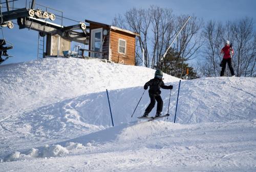A child skiing down a snowy slope, with a ski lift and another person in the background.