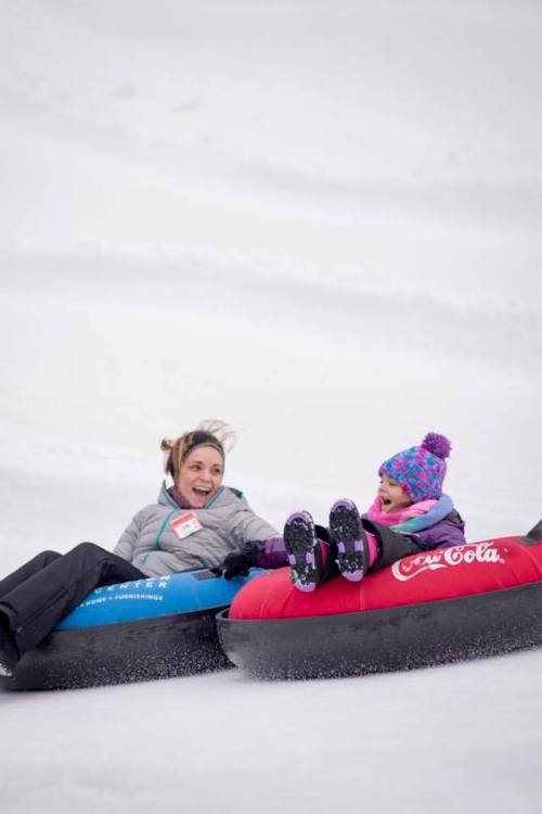 Two people enjoy snow tubing, laughing as they slide down a snowy hill on colorful inflatable tubes.