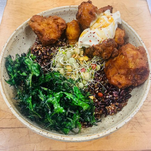 A bowl of black rice topped with fried chicken, sprouts, kale, and a dollop of sauce.