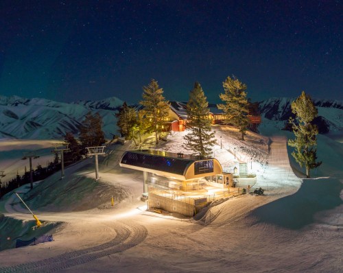 A ski resort at night, featuring a lodge and ski lift surrounded by snow-covered mountains and starry sky.