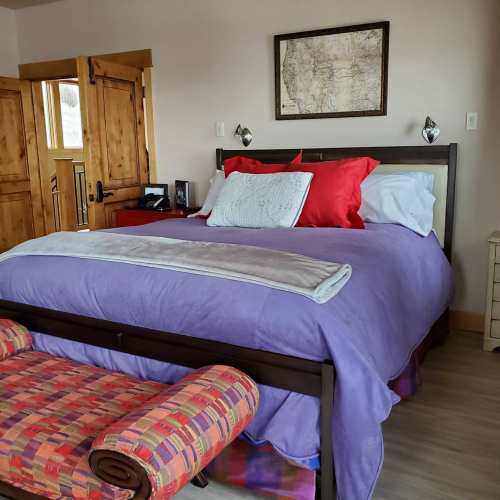 Cozy bedroom featuring a purple bedspread, red and white pillows, and wooden accents with a map on the wall.