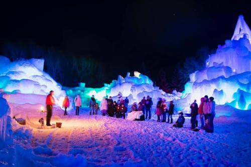 A winter scene with colorful ice formations and people gathered around a fire at night.