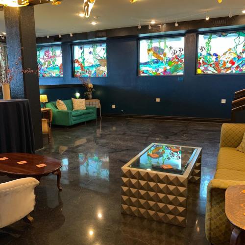 A stylish lounge with stained glass windows, green sofas, and a geometric coffee table on a polished floor.