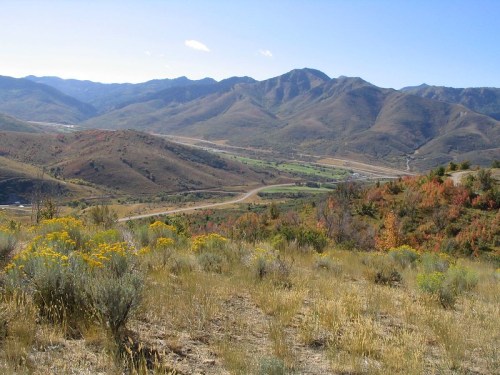 A scenic view of rolling mountains and valleys, with colorful autumn foliage and clear blue skies.