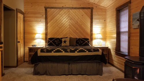 Cozy bedroom with wooden walls, a large bed with a star-patterned quilt, and warm lighting from bedside lamps.