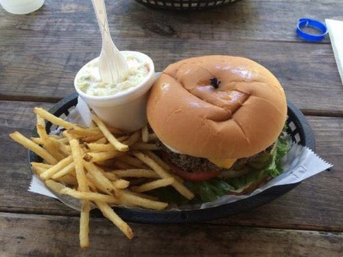 A burger with cheese, lettuce, and tomato, served with fries and a cup of coleslaw on a wooden table.