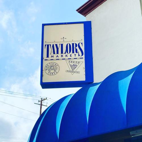 Sign for Taylor's Market featuring "Fresh Produce" and "Bioscience Tea," with a blue awning below.