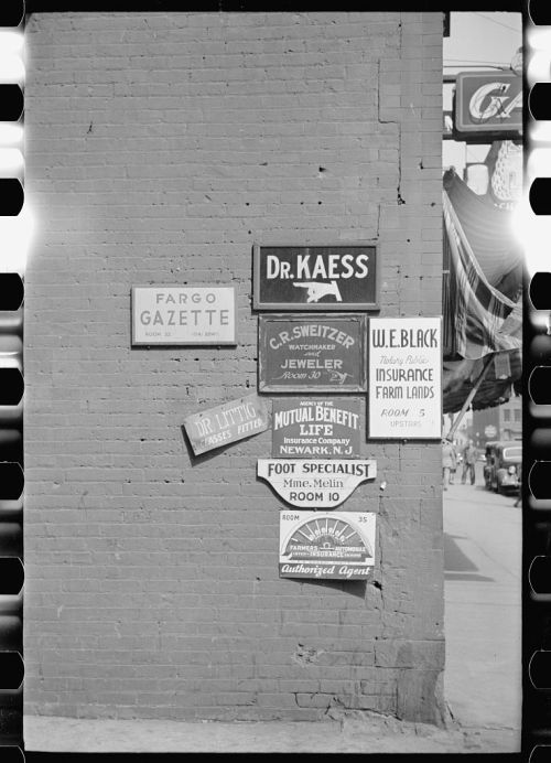 Signage on a brick wall featuring various business advertisements, including a newspaper and local services.