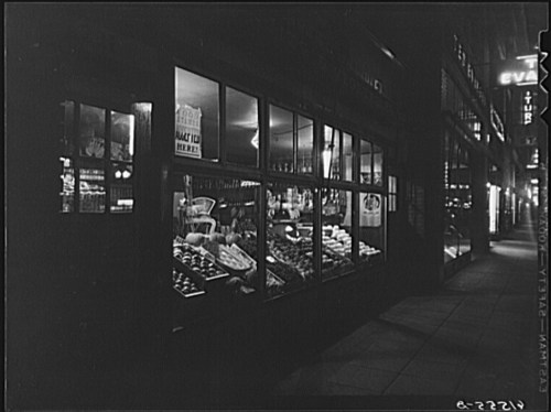 A dimly lit street scene featuring a shop window displaying various goods at night.