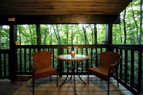A cozy balcony with two chairs and a table, surrounded by lush green trees in a serene forest setting.