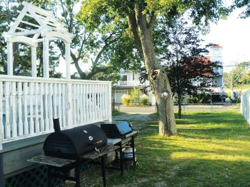 A backyard scene featuring a white gazebo, a grill, and trees, with a house visible in the background.