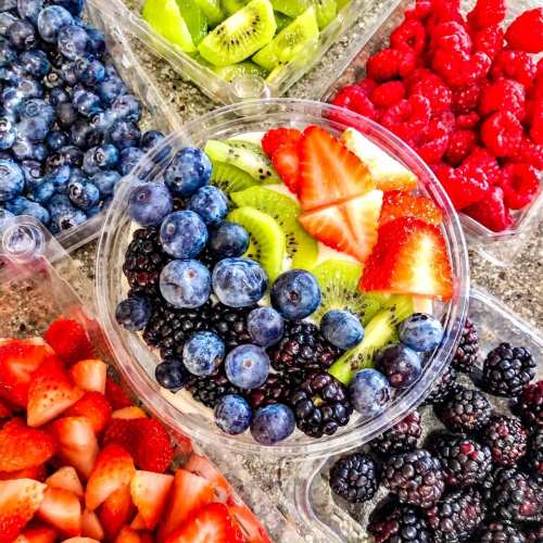 A colorful assortment of fresh berries and kiwi in clear containers, including strawberries, blueberries, blackberries, and raspberries.