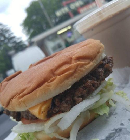 A close-up of a hamburger with lettuce, onion, and cheese, alongside a cup of iced coffee.