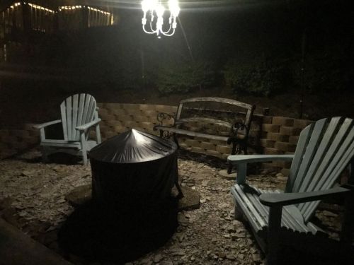 A dimly lit outdoor seating area at night with two blue chairs, a bench, and a covered fire pit.