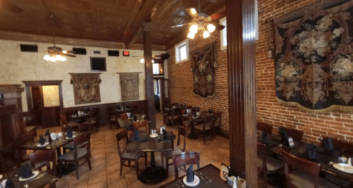 Interior of a cozy restaurant featuring brick walls, wooden tables, and decorative tapestries.
