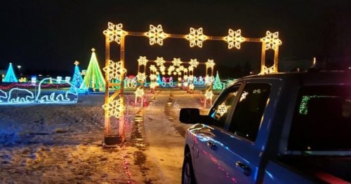 A car parked beside a colorful holiday light display featuring snowflakes, trees, and festive decorations at night.