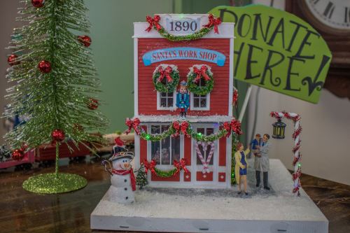 A festive model of Santa's workshop with decorations, a snowman, and a sign that says "Donate Here!" in the background.