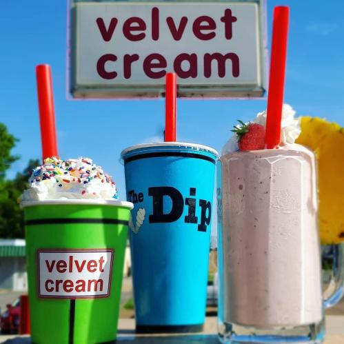 Three colorful ice cream drinks with whipped cream and toppings, displayed in front of a "Velvet Cream" sign.