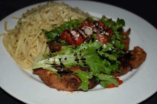 A plate featuring crispy chicken topped with fresh greens and tomatoes, served alongside a portion of pasta.