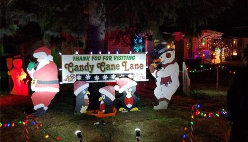 Colorful holiday decorations featuring Santa, penguins, and a snowman with a sign reading "Thank You for Visiting Candy Cane Lane."