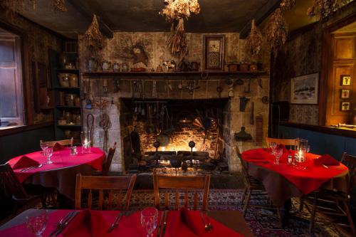 Cozy restaurant interior with a stone fireplace, wooden tables set for dining, and rustic decor featuring dried herbs.