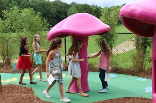 Children play around large pink mushroom structures in a colorful outdoor playground.