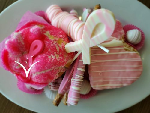 A plate of pink-themed desserts, including a donut, candy sticks, and various confections, all decorated in pink.