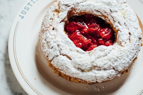 A round pastry topped with powdered sugar and filled with bright red strawberries on a white plate.