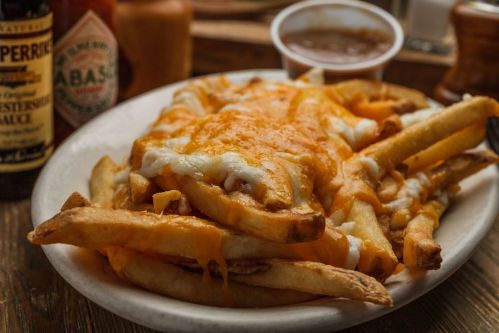 A plate of cheesy fries topped with melted cheese and served with a side of dipping sauce.
