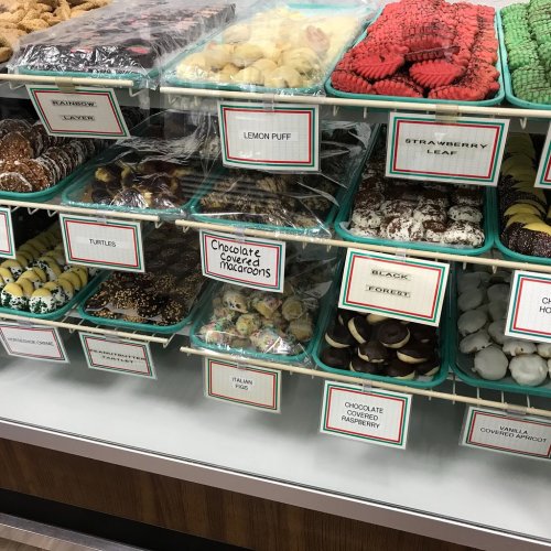 A display case filled with various colorful cookies and treats, labeled with names like "Lemon Puff" and "Chocolate Covered Macaroons."
