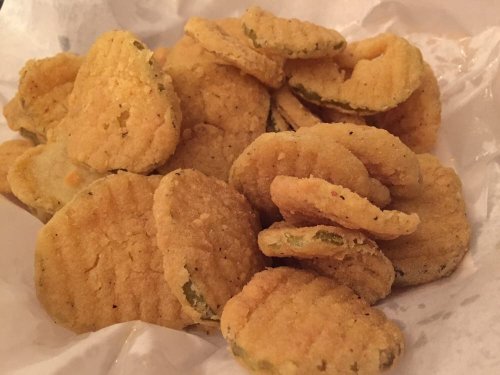 A pile of golden-brown, crispy fried pickles on a white paper background.