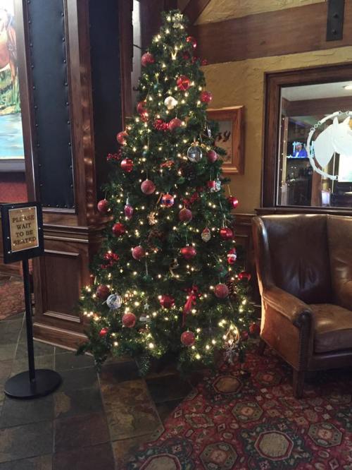 A decorated Christmas tree with red and gold ornaments, surrounded by a cozy seating area in a rustic setting.