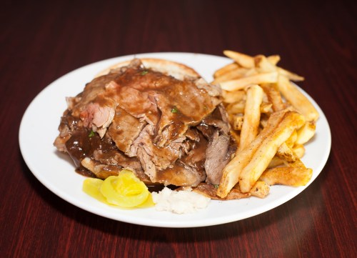 A plate of sliced roast beef with gravy, served with fries and lemon slices on the side.
