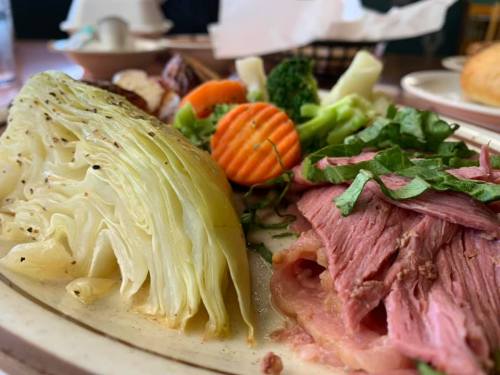 A plate featuring sliced corned beef, cooked cabbage, and a variety of steamed vegetables, including carrots and broccoli.