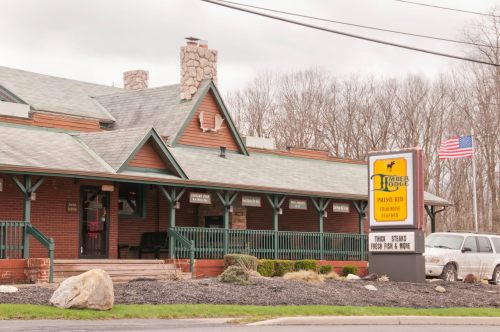 A rustic restaurant exterior with a stone chimney, green trim, and a sign advertising prime rib and seafood.