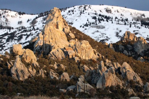 Rocky mountain landscape with snow-capped peaks and rugged formations under a cloudy sky.