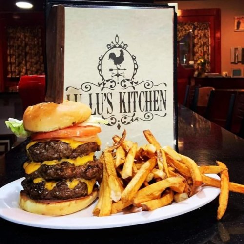 A towering cheeseburger with multiple patties, lettuce, and tomato, served with a side of golden fries.