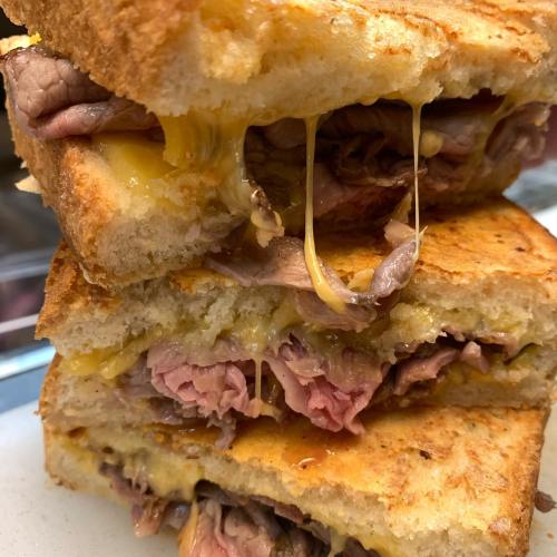 A stacked grilled cheese sandwich with layers of melted cheese and slices of roast beef, oozing with flavor.
