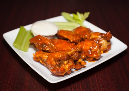 A plate of spicy chicken wings with celery sticks and a side of ranch dressing.