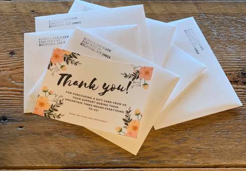 A thank you card with floral design on a wooden table, surrounded by white envelopes.