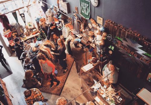 A bustling retail store with people browsing clothing and accessories, featuring a cozy, rustic interior.