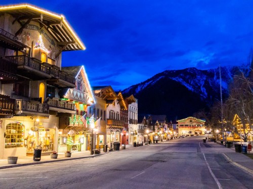 A charming street lined with festive buildings, illuminated at night, with mountains in the background.