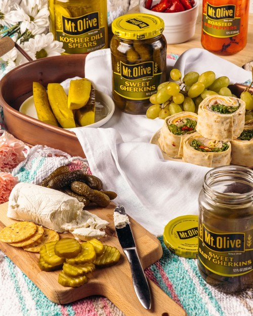 A colorful spread featuring pickles, cheese, crackers, and wraps, with Mt. Olive jars in the background.