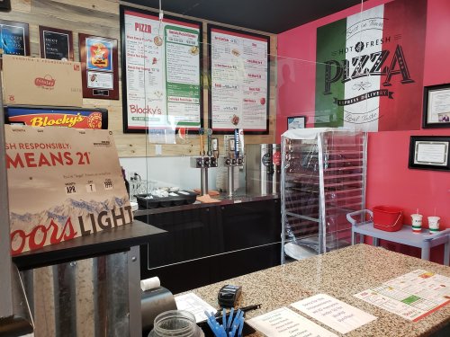 Interior of a pizza shop featuring a menu board, drink taps, and a counter with promotional signage.