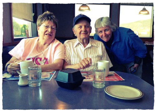 Three people sit at a table in a diner, smiling and enjoying their time together, with drinks and menus in front of them.